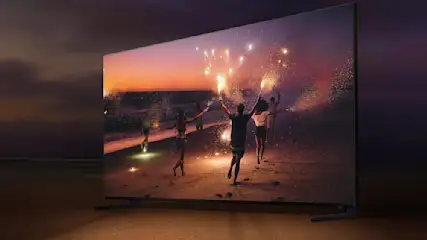 Ein Fernseher zeigt eine Gruppe von Menschen, die am Strand Wunderkerzen schwingen, mit einem Sonnenuntergang im Hintergrund.