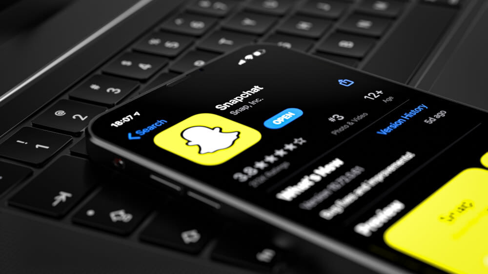 Ein iPhone, auf dessen Display Snapchat angezeigt wird, liegt auf einer Tastatur.