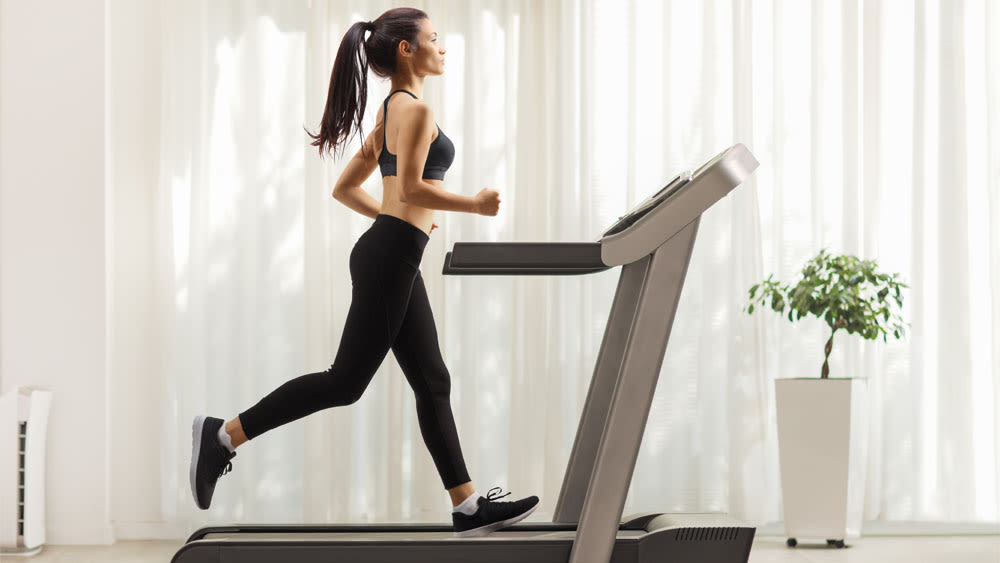 Eine Frau in Sportkleidung trainiert auf einem Laufband zu Hause.