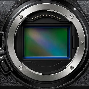 NIKON Z6III Gehäuse Systemkamera, 8 cm Display Touchscreen, WLAN Nahaufnahme einer Kameraöffnung mit silbernem Ring und sichtbarem, rechteckigem, grün-blauem Sensor. Schrauben sind sichtbar.