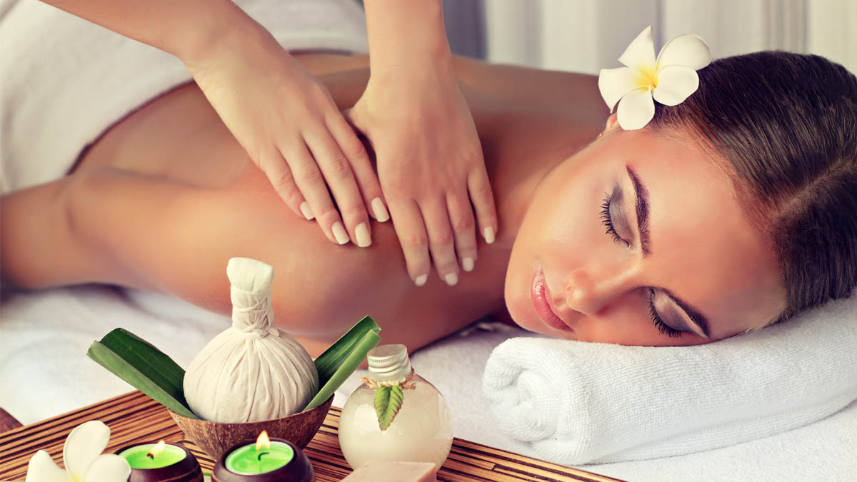 Eine Frau liegt auf einer Liege und bekommt eine Rückenmassage. Kerzen und Blumen dekorieren den Raum.