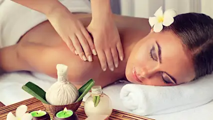 Eine Frau liegt auf einer Liege und bekommt eine Rückenmassage. Kerzen und Blumen dekorieren den Raum.