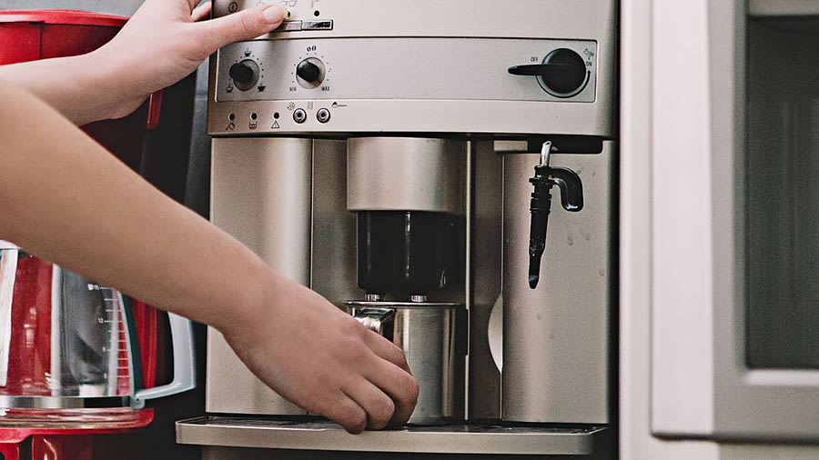 Eine Person stellt eine Tasse unter einen Kaffeevollautomaten und bedient diesen.