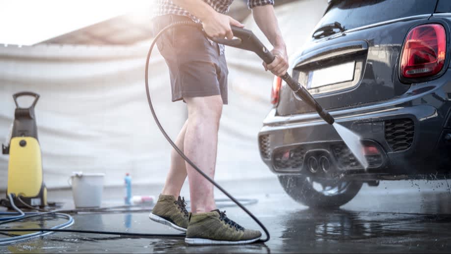 Ein Mann putzt sein Auto mit einem Hochdruckreiniger.