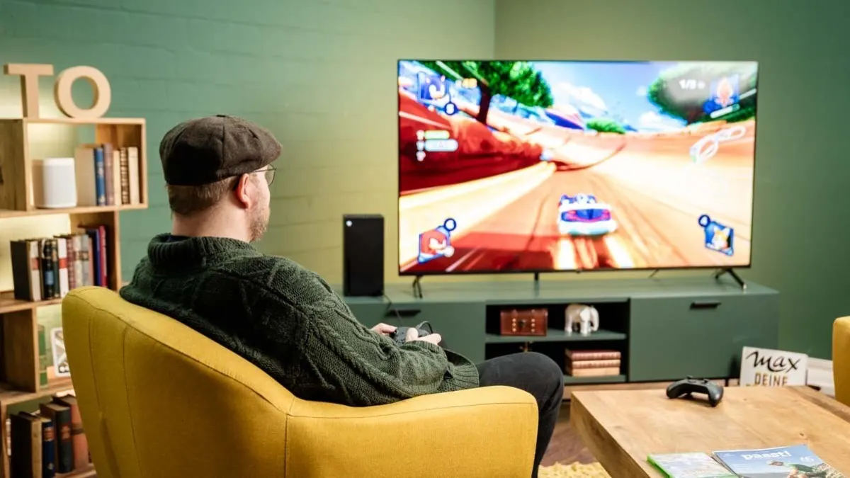 TURN ON Redakteur Andreas sitzt auf einem Sessel und spielt ein Rennspiel an einem OLED-TV, neben dem eine Xbox Series X steht.