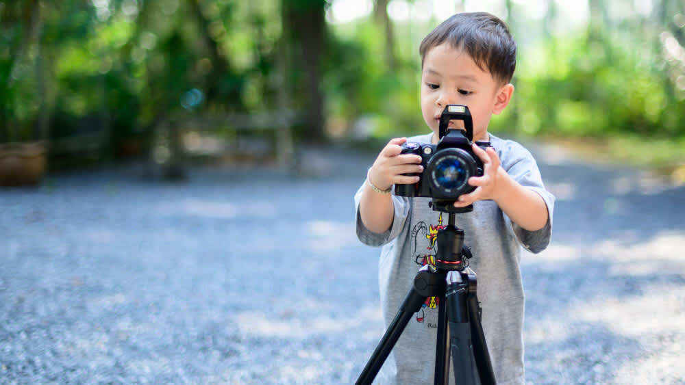 Ein kleiner Junge bedient auf einem Schotterweg eine Kamera.