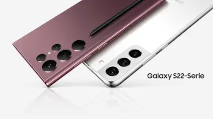 Zwei Samsung Galaxy S22-Serie Smartphones in Weiß und Rosé, mit Kameras und einem schwarzen Stift auf weißem Grund.