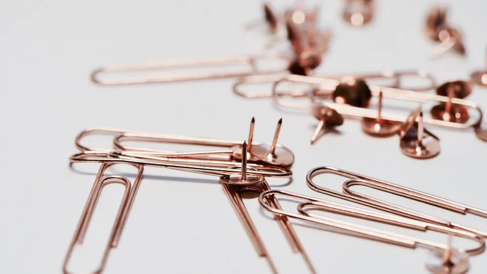 Auf weißem Grund liegen Büroklammern und Reißzwecken aus Metall. Die Objekte sind unsortiert und teilweise überlappend.