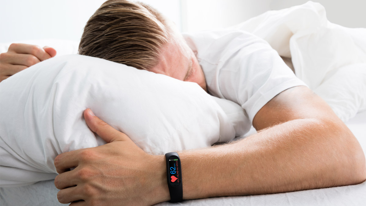 Eine Person schläft in einem Bett unter einer grauen Decke, mit einem weißen Kissen unter dem Kopf.