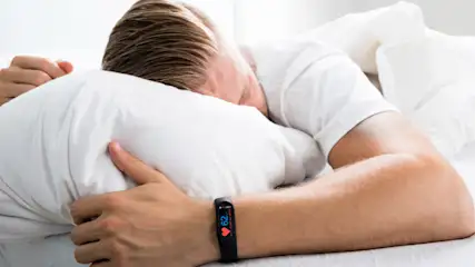 Eine Person schläft in einem Bett unter einer grauen Decke, mit einem weißen Kissen unter dem Kopf.