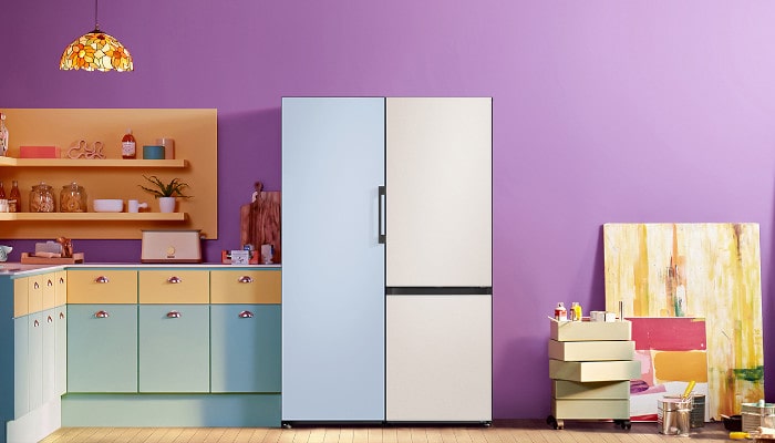 Eine Küche mit pastellfarbenen Schränken, einem zweifarbigen Kühlschrank und einem Regal. Eine Lampe hängt über einem violetten Hintergrund.