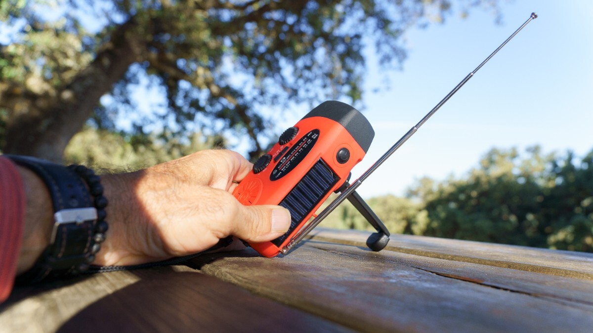 Ein Mann stellt ein Kurbelradio mit ausgefahrener Antenne auf einen Tisch im Freien.