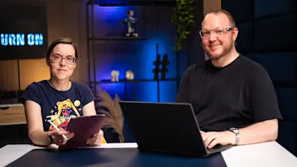 Daniela (links) hält ein iPad und einen Apple Pencil in den Händen und Andreas (rechts) tippt auf einem Laptop.