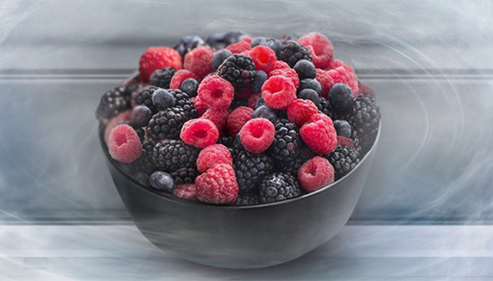 Eine dunkle Schale ist gefüllt mit roten Himbeeren, blauen Heidelbeeren und schwarzen Brombeeren.