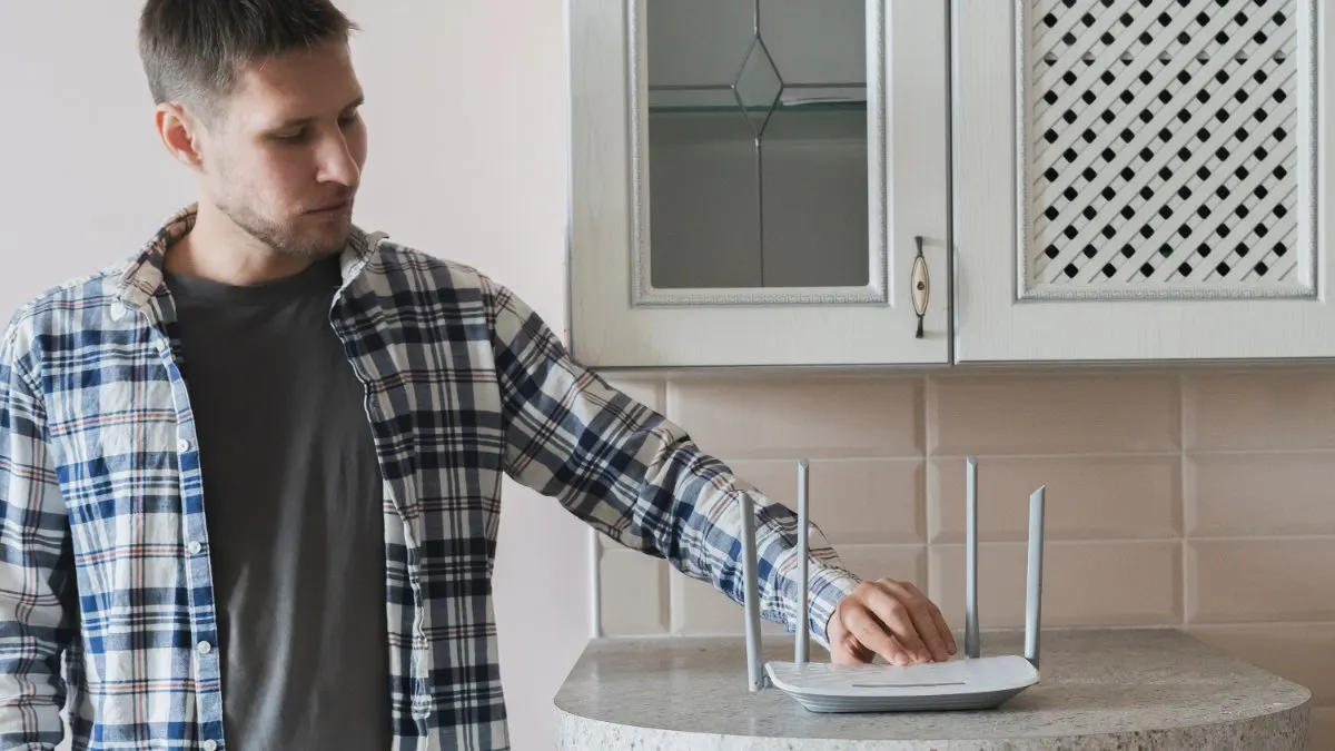 Ein Mann steht vor einem Internetrouter und berührt ihn.