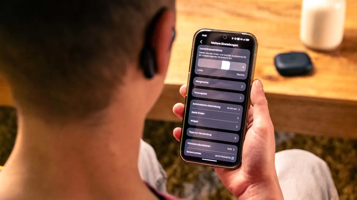 Alex trägt die Soundcore Aerofit 2 und schaut auf sein Smartphone, auf dem die Soundcore-App geöffnet ist.