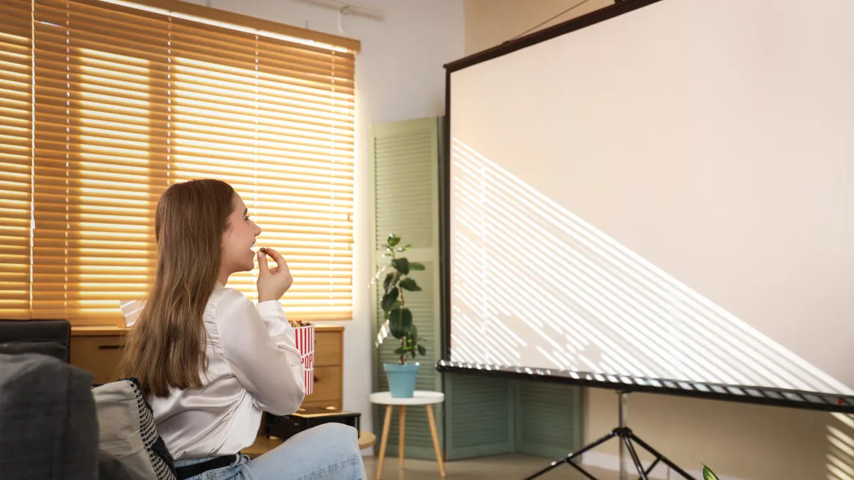 Eine Frau sitzt im Wohnzimmer vor einer Beamer-Leinwand.