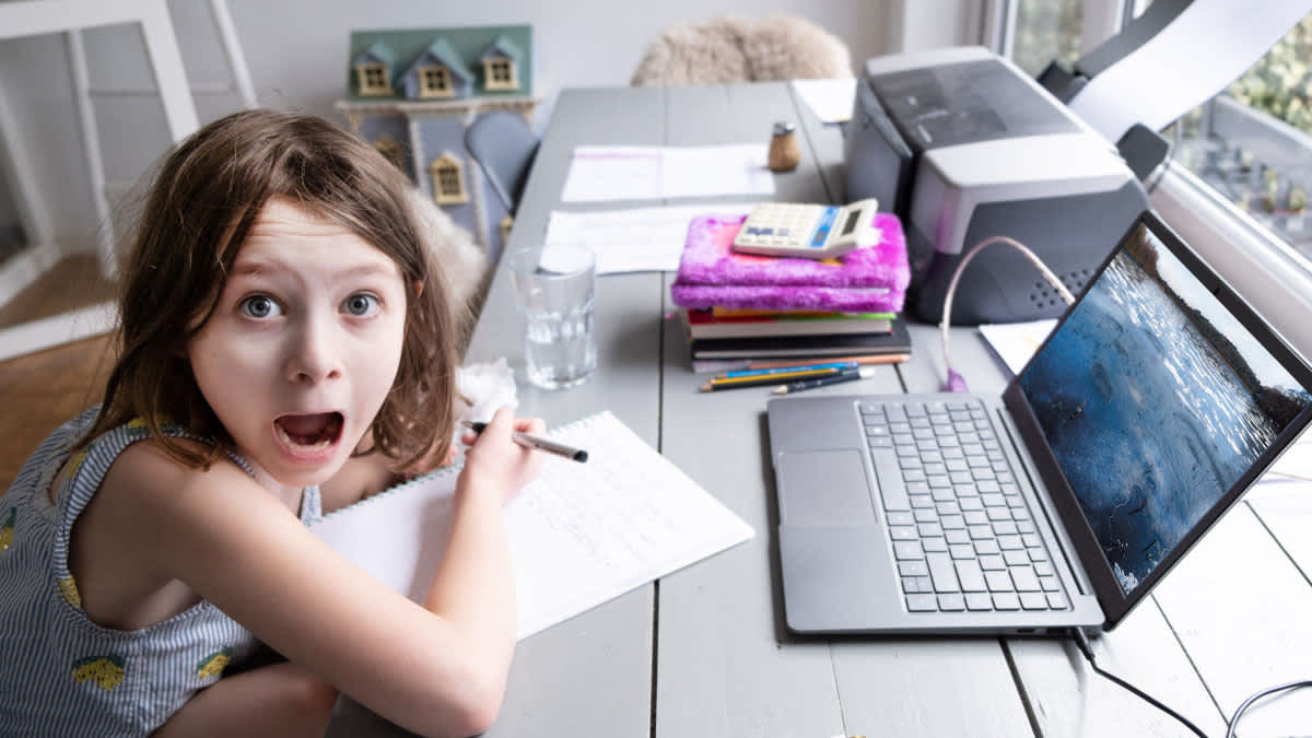 Ein Kind sitzt mit Laptop an einem Schreibtisch.