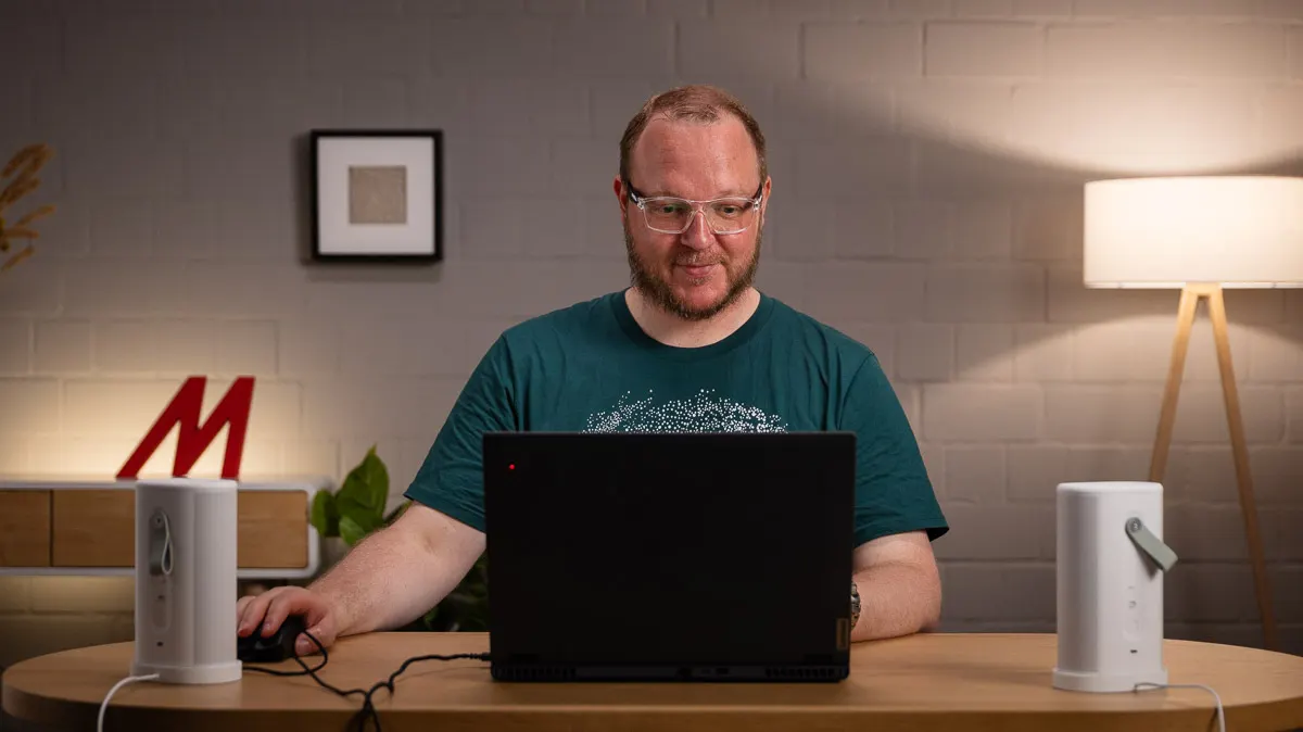 Andreas schaut auf einen Laptop, links und rechts auf dem Tisch stehen Sonos-Play-Lautsprecher.