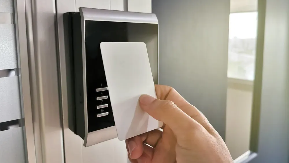 Hand hält weiße Karte vor elektronisches Schloss an einer Tür. Das Schloss ist silberfarben und schwarz.