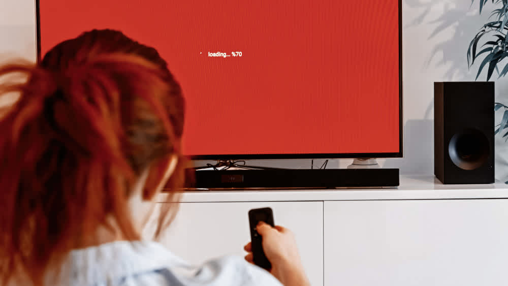 Eine Frau vor einem TV mit Soundbar-Fernbedienung in der Hand