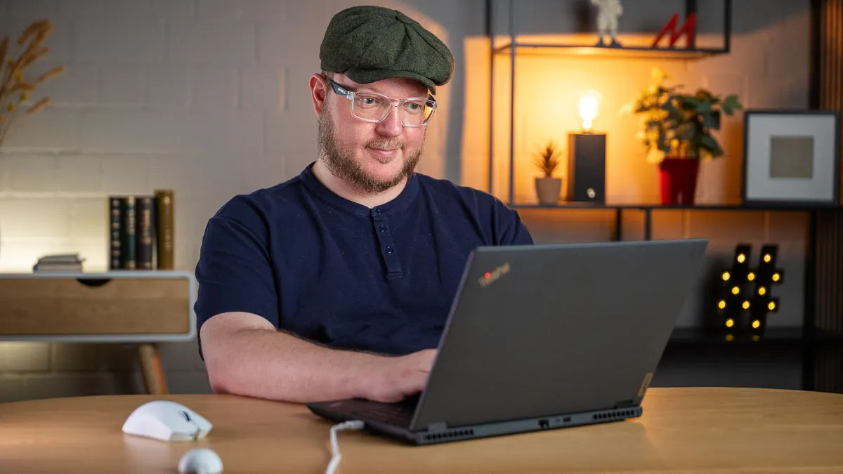 Andreas sitzt vor einem schwarzen ThinkPad, an das ein weißer USB-Dongle mit einem Kabel angeschlossen ist. Neben ihm liegt die kabellose Razer Viper V4 Pro.