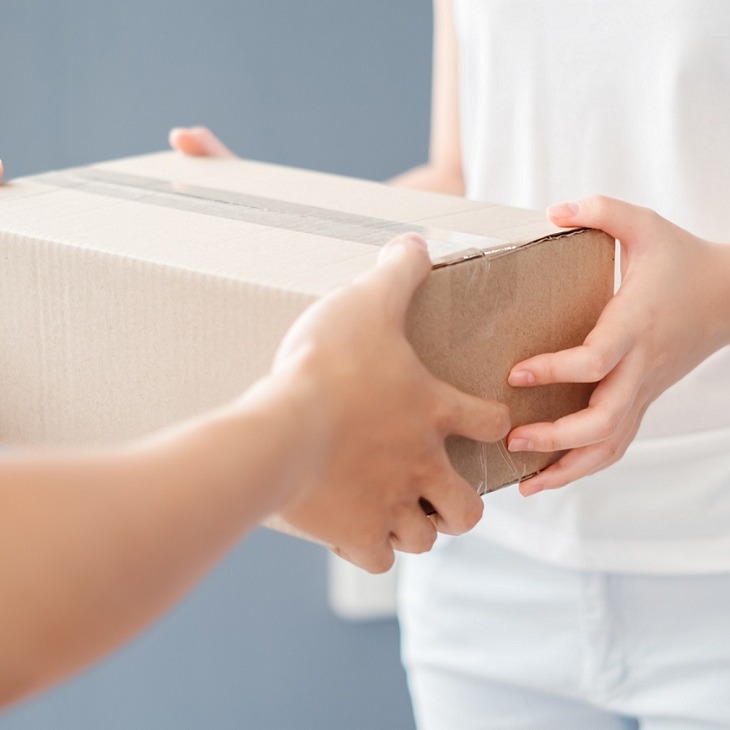 Eine Person übergibt einer anderen ein Paket in einem neutralen, hellen Raum.