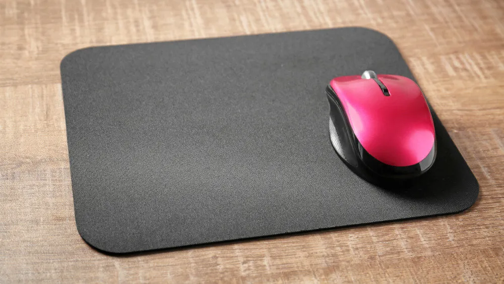 Ein graues Mousepad liegt auf einem Holztisch, darauf eine rot-schwarze Computermaus.