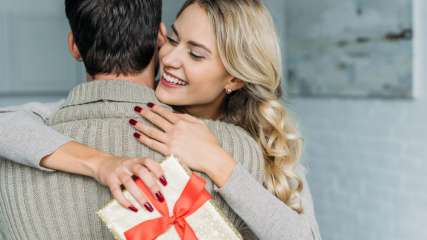 Eine Frau mit einem Geschenk in der Hand umarmt einen Mann.