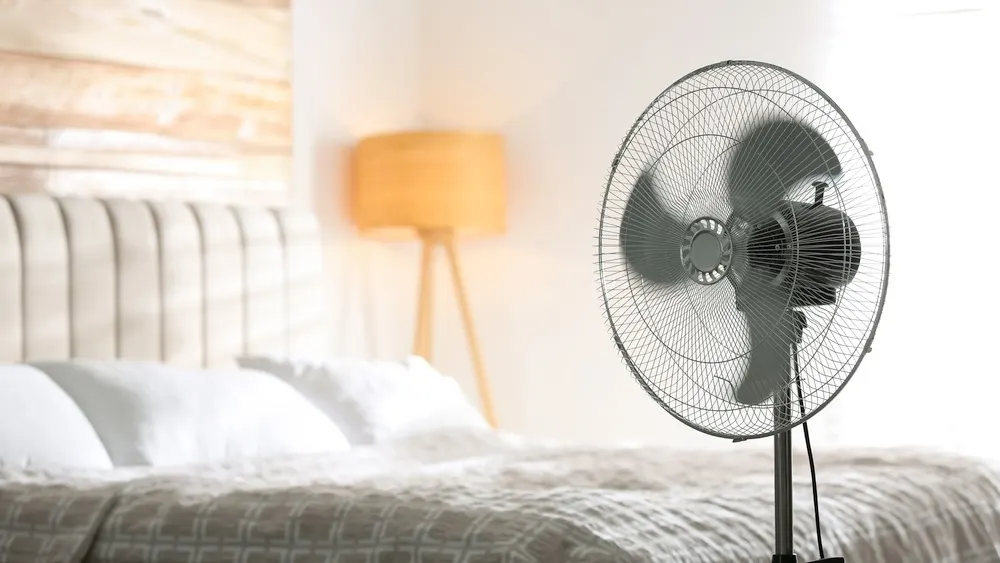 Ein Ventilator steht neben einem Bett.