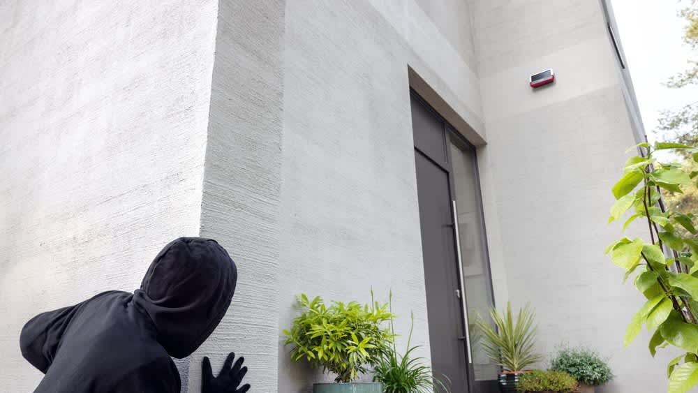 Ein Einbrecher versteckt sich vor der Bosch Smart Home Außensirene.