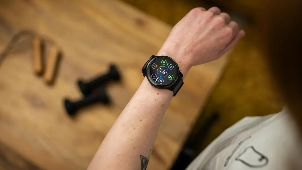 Franzi schaut auf den Homescreen der Garmin Venu 3, im Hintergrund liegen Kurzhanteln.
