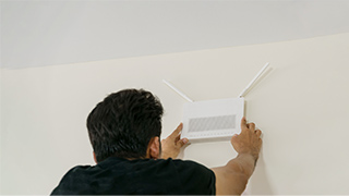 Mann in schwarzem Hemd montiert eine weiße rechteckige Platte an einer weißen Wand.