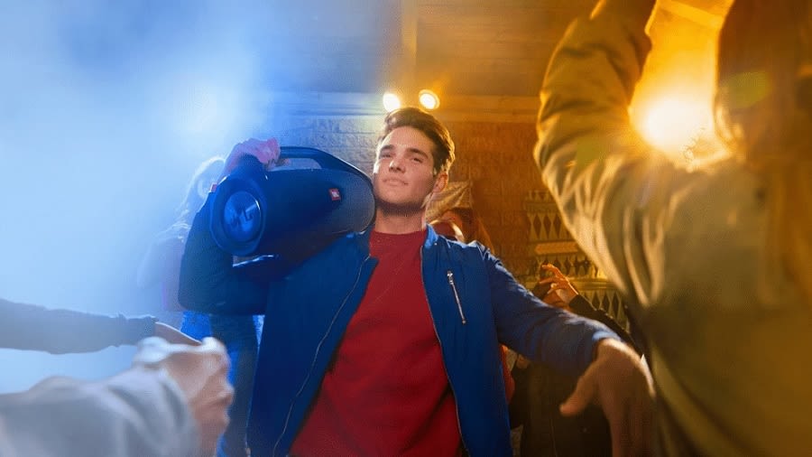 Ein junger Mann auf einer Party trägt einen JBL Boombox 2 Bluetooth Lautsprecher in Schwarz auf den Schultern