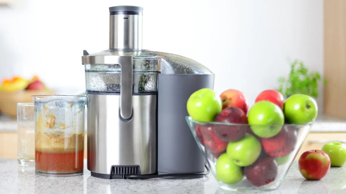 Ein Zentrifugalentsafter steht mit einer Schüssel Äpfeln auf einer Arbeitsplatte in einer Küche.