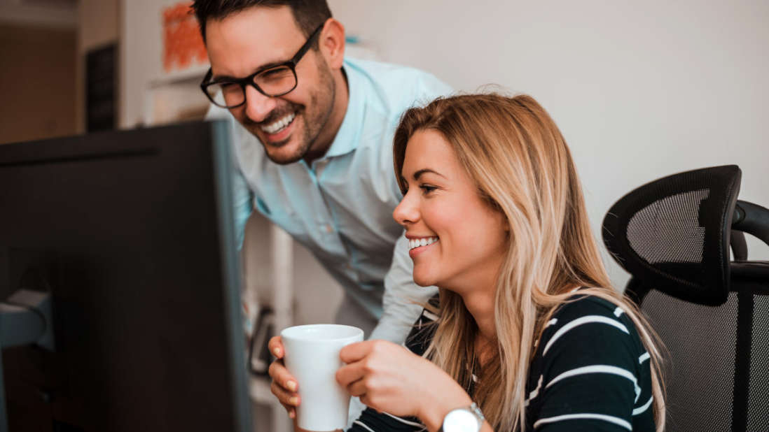 Zwei Personen lachen gemeinsam vor einem Computer.