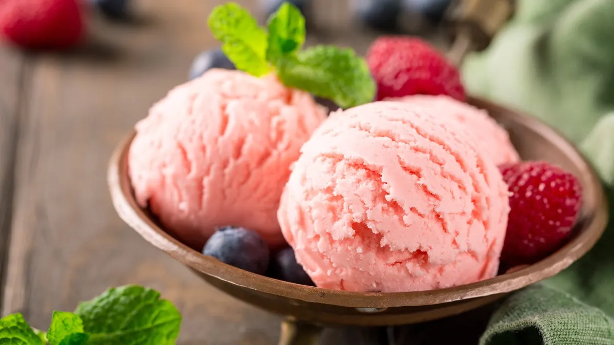 Mehrere Kugeln Erdbeereis sind mit Beeren und Minze in einer Holzschüssel angerichtet.