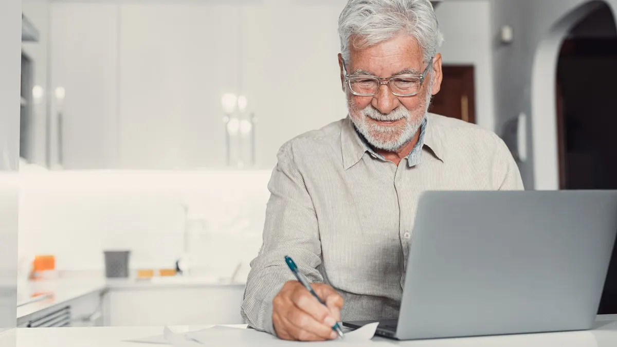 Ein älterer Mann sitzt mit einem Laptop am Küchentisch.