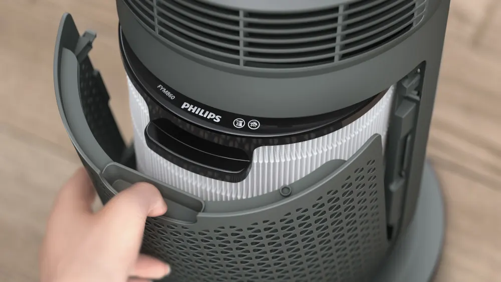 Ein grauer Philips Luftreiniger wird geöffnet, um den weißen Filter freizulegen. Die Hand hält eine perforierte Abdeckung.