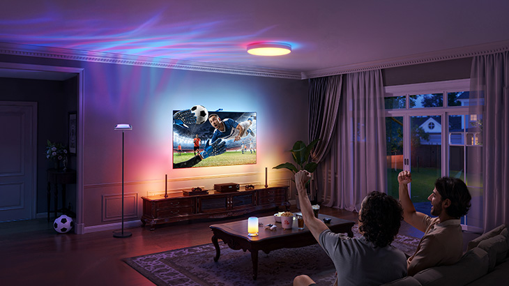 Modernes Gaming-Wohnzimmer mit großem TV, bunter LED-Beleuchtung, Smartphone-Steuerung und Sprachassistent-Nachricht. 