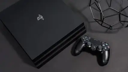 Auf einem schwarzen Tisch liegen eine schwarze Spielkonsole, ein Controller und eine geometrische Drahtdekoration.