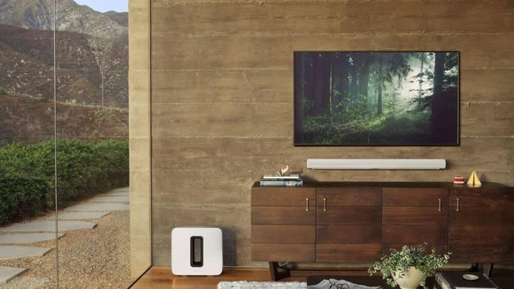 Sonos-Soundbar Arc unter einem TV in einem Wohnzimmer, daneben Sonos Sub