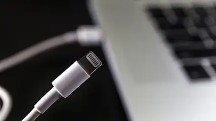 Nahaufnahme eines weißen Lightning-Kabels vor einem Laptop auf einem dunklen Hintergrund.