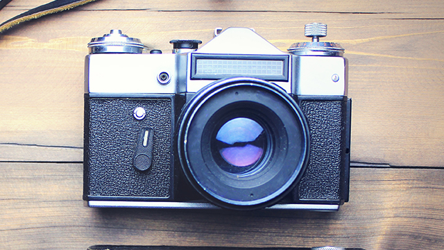 Eine silberne und schwarze Vintage-Kamera liegt auf einem hellbraunen Holztisch.
