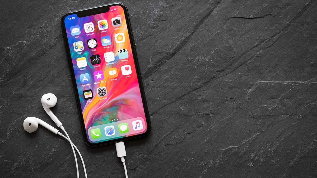Ein Smartphone liegt neben weißen Kopfhörern, die an das iPhone angeschlossen sind. Man sieht mehrere App-Icons auf dem Bildschirm.