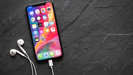 Ein Smartphone liegt neben weißen Kopfhörern, die an das iPhone angeschlossen sind. Man sieht mehrere App-Icons auf dem Bildschirm.