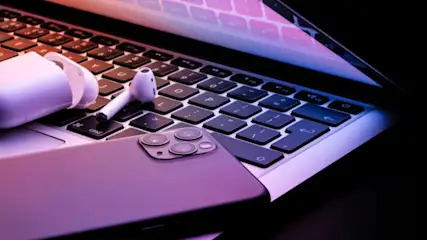 Auf einem Laptop liegen Kopfhörer und ein Handy. Die Tastatur des Laptops ist sichtbar.