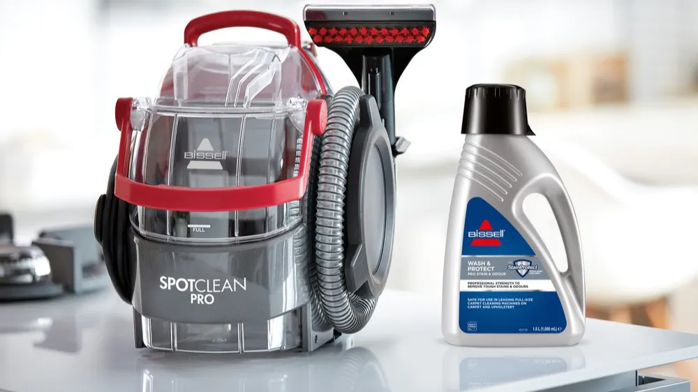 Ein Bissell SpotClean Pro Teppichreiniger und eine Flasche Reinigungsflüssigkeit stehen auf einer hellen Oberfläche.