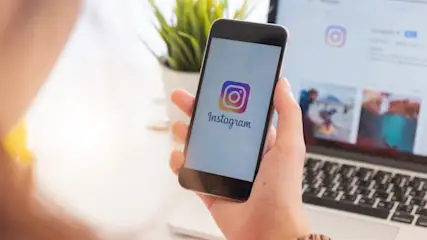 Eine Person hält ein Smartphone in der Hand, während auf dem Display das Instagram-Logo angezeigt wird.