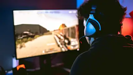 Person mit Kopfhörern vor einem Computerbildschirm, der eine Wüstenlandschaft in einem Videospiel zeigt.